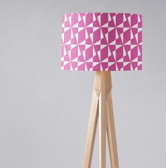 a pink and white lampshade on a wooden tripod with a light shade