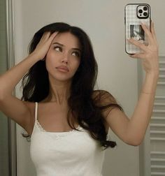 a woman holding up her cell phone to take a selfie in front of the mirror