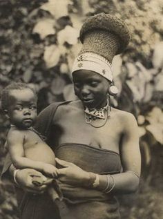 an old photo of a woman holding a baby in her arms and wearing a headdress