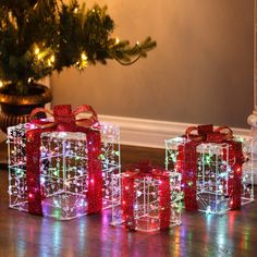 three presents are wrapped in red and green lights on the floor next to a christmas tree