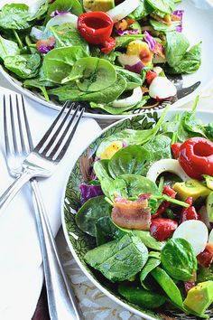 two white bowls filled with salad on top of a table next to utensils