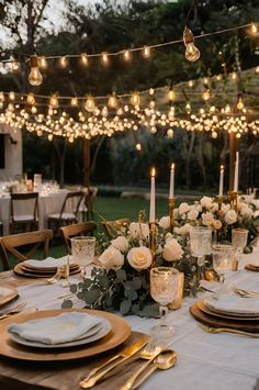 an outdoor dinner table set with candles, plates and place settings for guests to eat