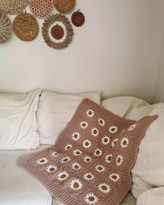 a crocheted blanket sitting on top of a couch next to pillows and plates