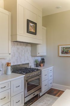 a kitchen with white cabinets and stainless steel stove top oven in the center of the room