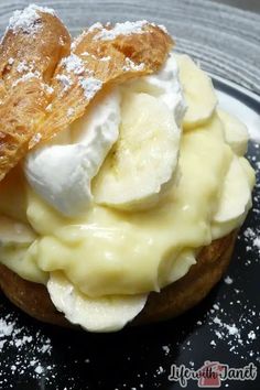 a pastry with bananas and whipped cream on top is sitting on a black plate covered in powdered sugar