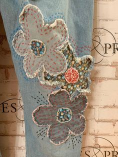 a pair of jeans with flower appliques on the back and side, hanging against a brick wall