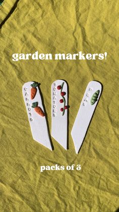 three white wooden spoons sitting on top of a green cloth covered table with the words garden markers