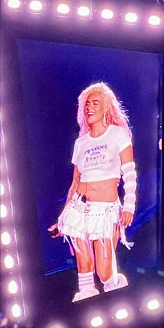 a woman in a white shirt and skirt standing on stage with lights around her head