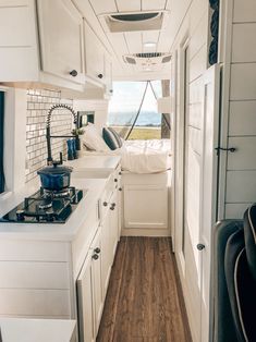 the interior of a camper with white cabinets and wood flooring, along with an open kitchen area