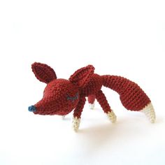 a knitted red and white toy animal on a white surface with its tail extended