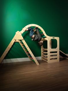 a young child climbing on a wooden slide in a play room with green walls and hardwood flooring