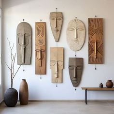 several wooden masks hanging on the wall above a table with vases in front of it