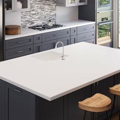 a modern kitchen with white counter tops and wooden stools in front of the sink