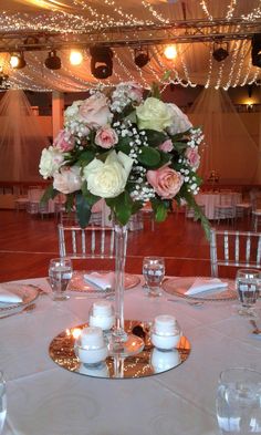 a vase filled with white and pink flowers on top of a table covered in candles