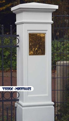 a tall white clock sitting next to a black fence and trees in the back ground