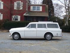 an old white station wagon parked in front of a red house