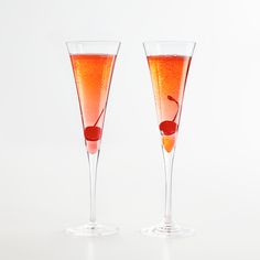 two champagne flutes with cherries in them on a white surface, side by side