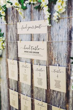 seating cards are hung on a wooden wall with white flowers and greenery around them