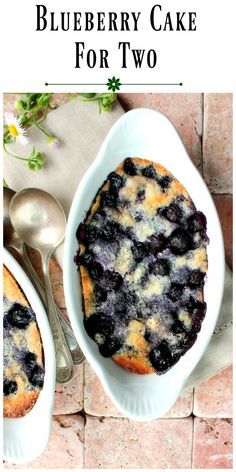 a blueberry cobbler in a white dish next to two spoons