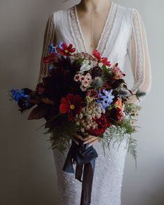 a woman holding a bouquet of flowers in her hands and wearing a white dress with sheer sleeves