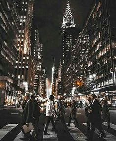 people crossing the street at night in new york city, with skyscrapers lit up