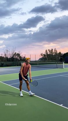 a man holding a tennis racquet on top of a tennis court at sunset