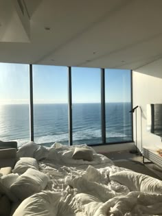 an unmade bed is in front of large windows overlooking the ocean and beach side