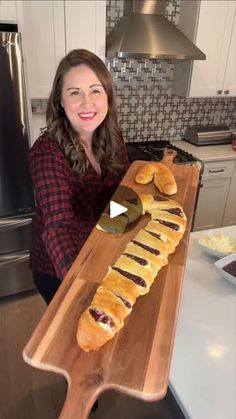 a woman standing in front of a wooden cutting board holding a long loaf of bread