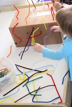 a young boy is playing with some colored sticks and paper on the table in front of him