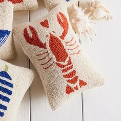 four pillows with lobsters on them sitting next to sea shells and seashells