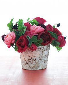 a flower pot filled with lots of flowers on top of a wooden table next to a white wall