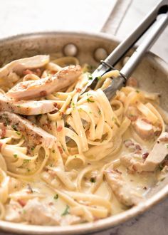 chicken alfredo in a skillet with two tongs