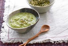 two bowls filled with green food on top of a purple place mat next to a wooden spoon