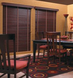 a dinning room table and chairs in front of two windows with blinds on them