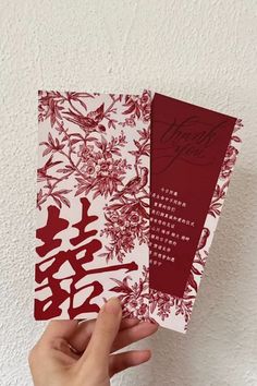 two red and white cards are held up in front of a wall with chinese writing on them