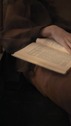 a person sitting down reading a book with their hand on the open book and holding it