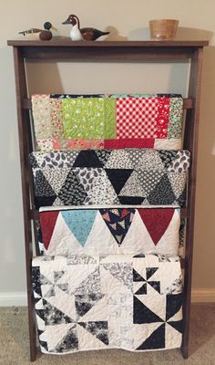 a rack with several quilts on it in the corner next to a wall mounted shelf