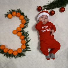 a baby is laying on the floor next to an orange wreath and christmas decorations that spell out happy new year