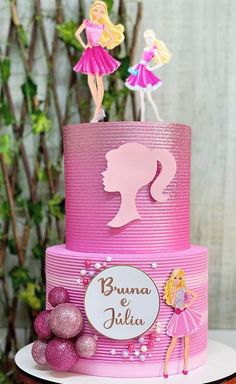 a pink birthday cake with barbie dolls on top