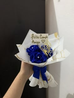 a person holding a bouquet of flowers in front of a white wall with the words feliz cumple amigo written on it