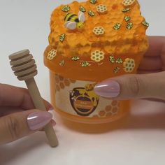 a hand holding a wooden toothbrush next to a honey jar with bees on it