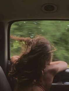 a woman sitting in the passenger seat of a car looking out the window at trees