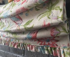 a close up of a window curtain with flowers on it and a brick wall in the background