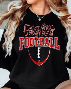 a woman sitting on top of a bed wearing a black shirt with the words eagles football printed on it