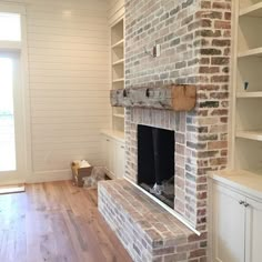 an empty living room with a brick fireplace and built - in shelving units on either side