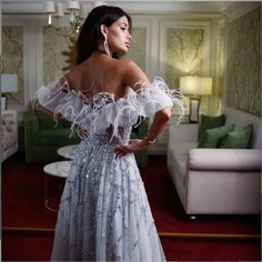 a woman in a white dress is standing near a couch and looking off to the side