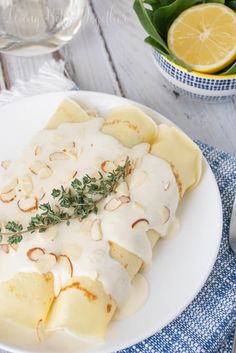 a white plate topped with ravioli covered in gravy and garnished with herbs