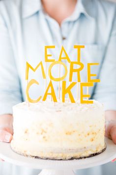 a woman holding a cake with the words eat more cake on it and yellow candles