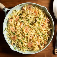 pasta with shrimp and parsley in a skillet next to a spatula on a wooden table