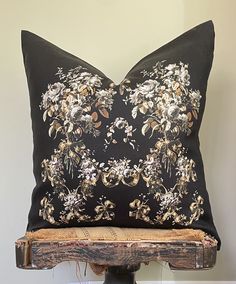 a black pillow with gold and white flowers on it sitting on a wooden shelf next to a wall